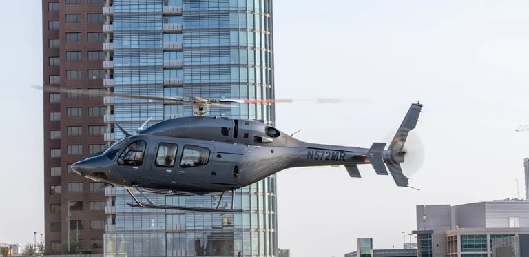 A gray helicopter flying in front of modern city buildings with glass and brick facades