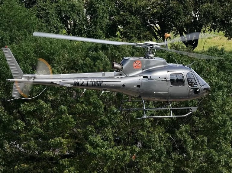 Silver helicopter with red star insignia flying over dense green forest canopy in daylight