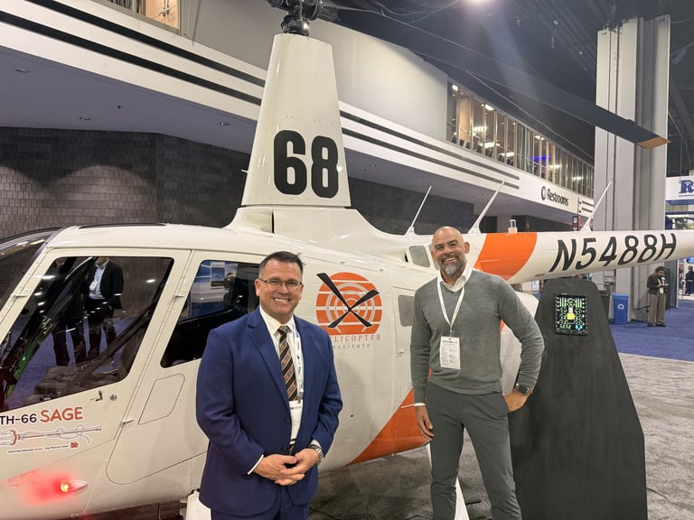 Two men stand in front of a white and orange helicopter numbered 68 at an indoor aviation event.